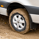 a close-up photo of the left rear wheel of a 2023 mercedes benz sprinter awd van. the van is driving on a muddy trail; the tire is completely caked in mud.